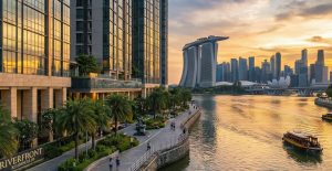 An elegant luxury riverfront residential tower in Singapore’s District 9 at sunset, with reflective glass façade overlooking the Singapore River, lush greenery around, and a vibrant urban skyline beyond.